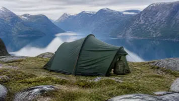 Grønt enmannstelt med ryggsekk på en fjellhylle over fjorden
